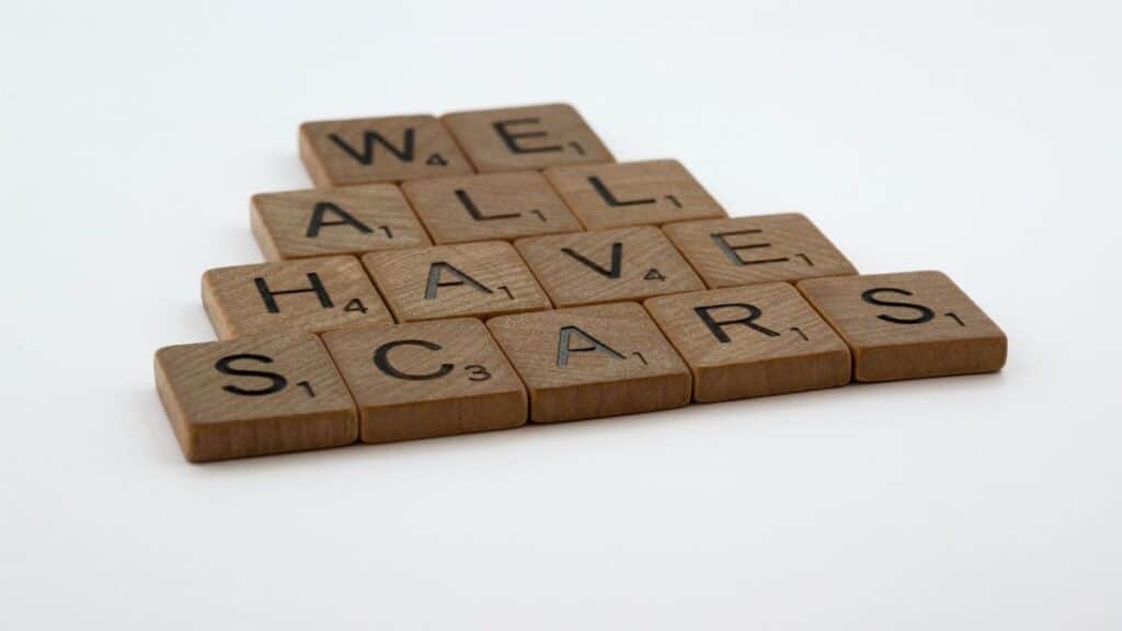 Wooden letter tiles arranged to spell 'we all have scars' on a white background.
