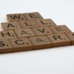 Wooden letter tiles arranged to spell 'we all have scars' on a white background.