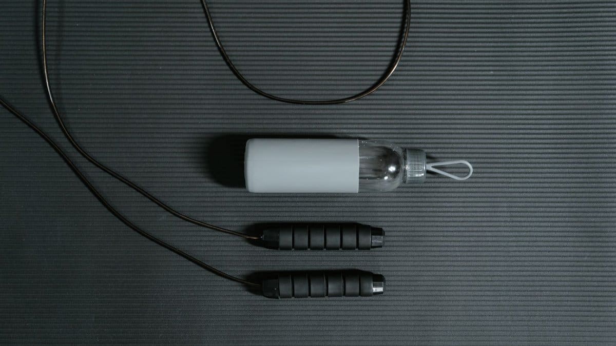 Flat lay of jump rope and water bottle on a yoga mat for fitness and hydration.