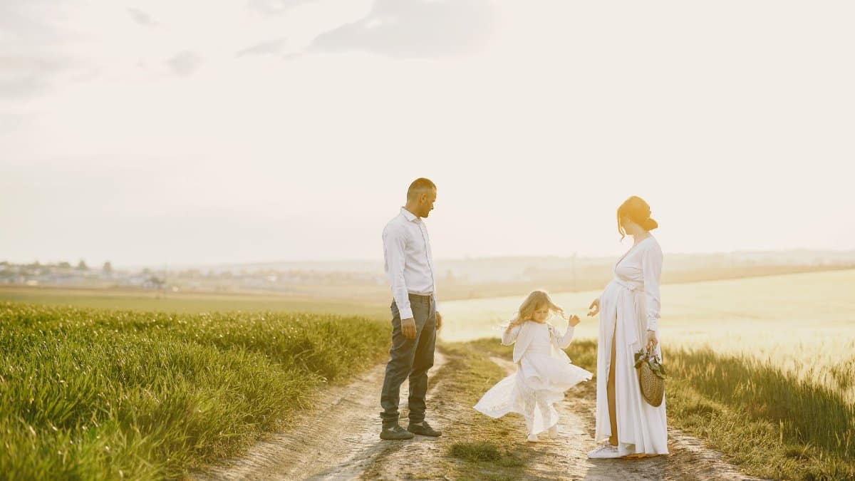A pregnant woman with her family walking along a scenic dirt road in the countryside at sunset.