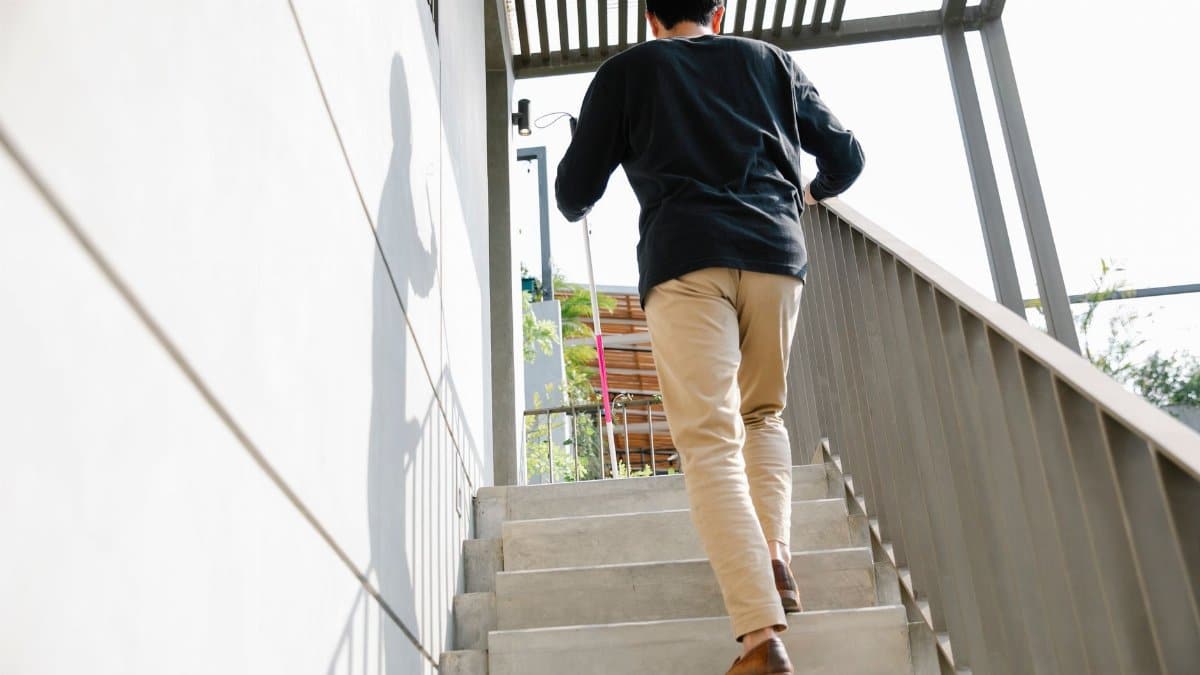 A man is seen walking up an outdoor staircase on a sunny day, casting a shadow on the wall.