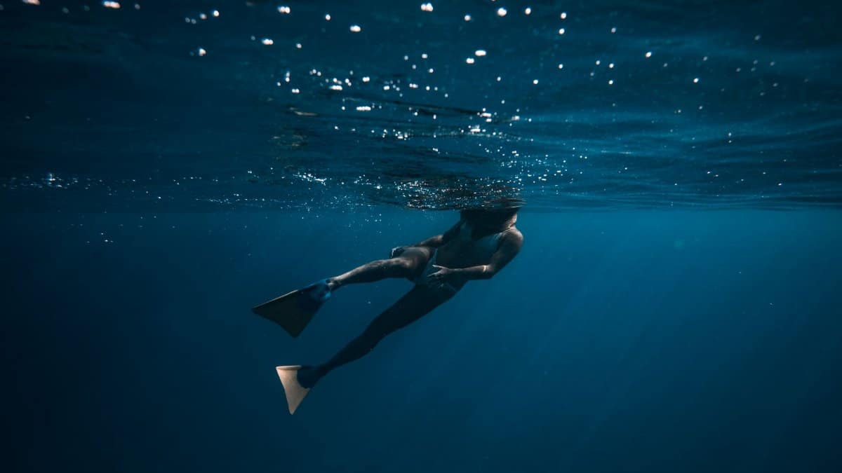A breathtaking underwater shot of a freediver swimming in deep blue ocean waters.