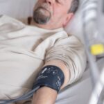 Elderly man resting in hospital bed with blood pressure monitor attached, symbolizing healthcare and medical care.