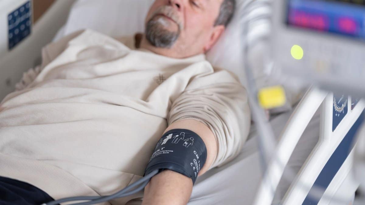 Elderly man resting in hospital bed with blood pressure monitor attached, symbolizing healthcare and medical care.