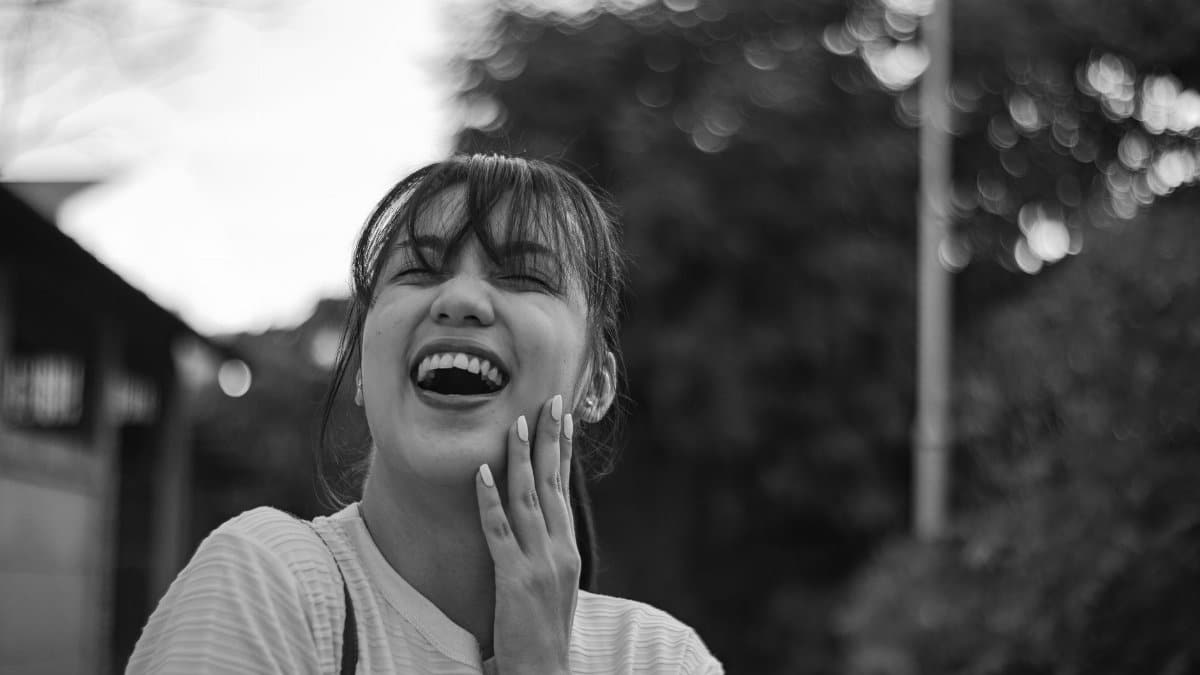 Cheerful young woman laughing outdoors in grayscale portrait.