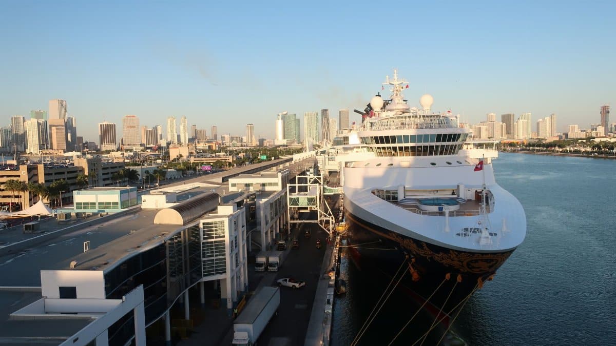 Aerial view of a cruise ship docked at Miami Beach port with a city skyline backdrop.
