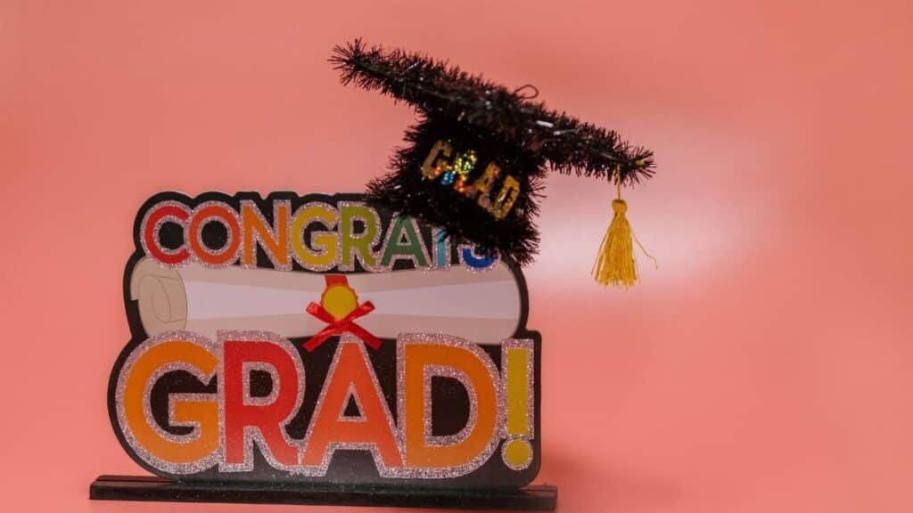 Celebratory 'Congrats Grad' sign with a glittery graduation cap on pink background.