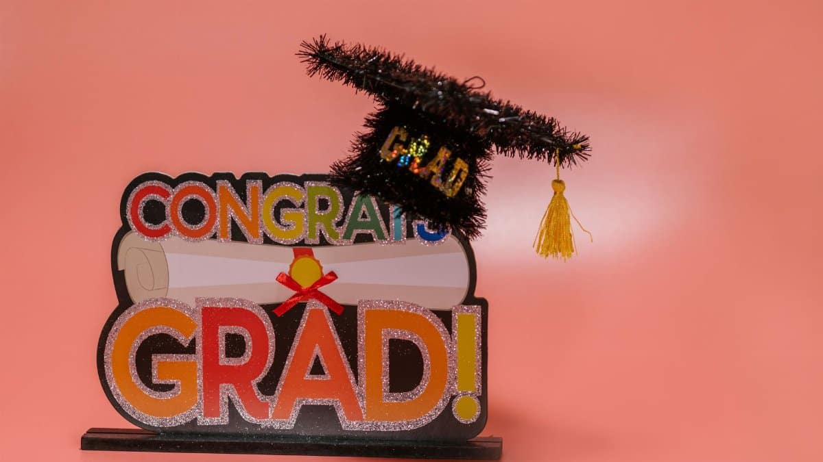 Celebratory 'Congrats Grad' sign with a glittery graduation cap on pink background.