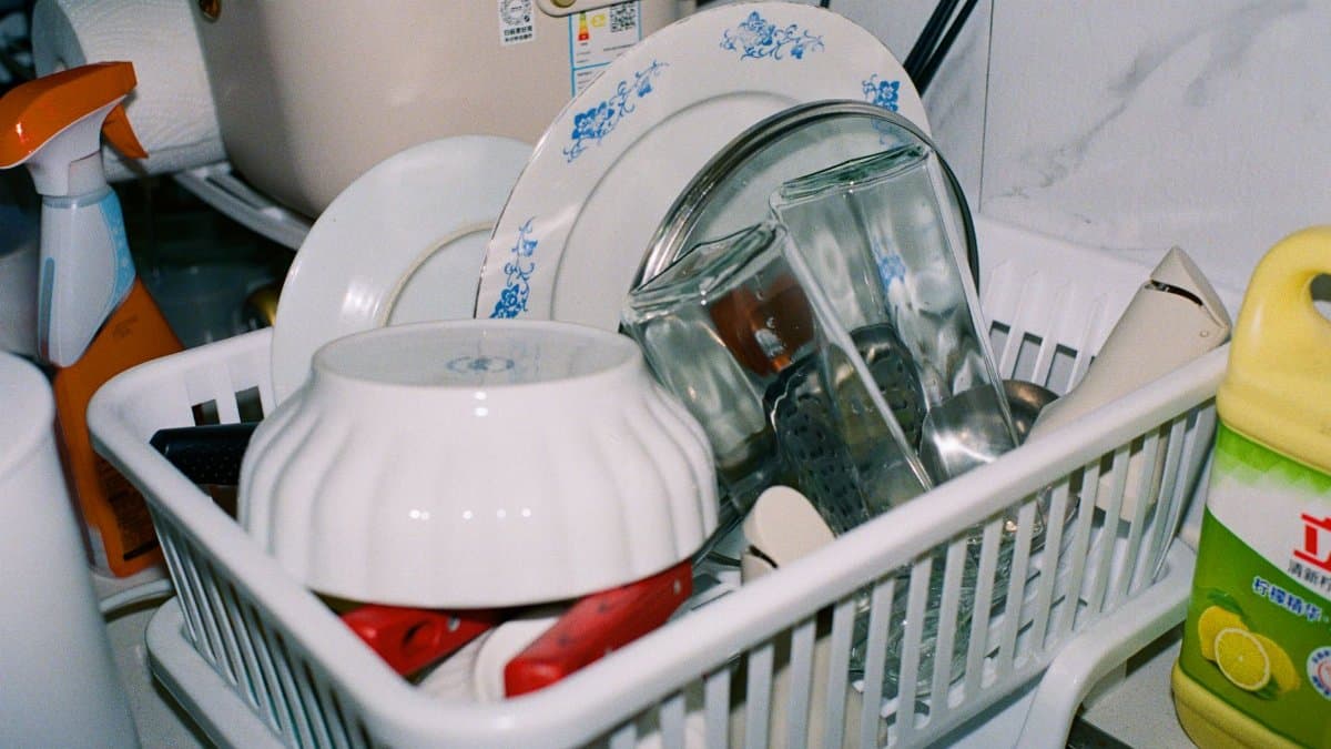 Clean kitchenware including plates and glasses drying in a dish rack with cleaning supplies nearby.