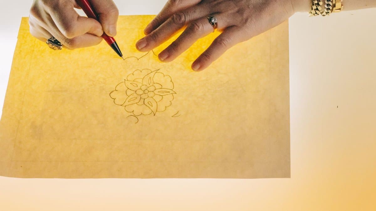 Hands tracing a floral design on backlit paper, showcasing artistic craftsmanship.