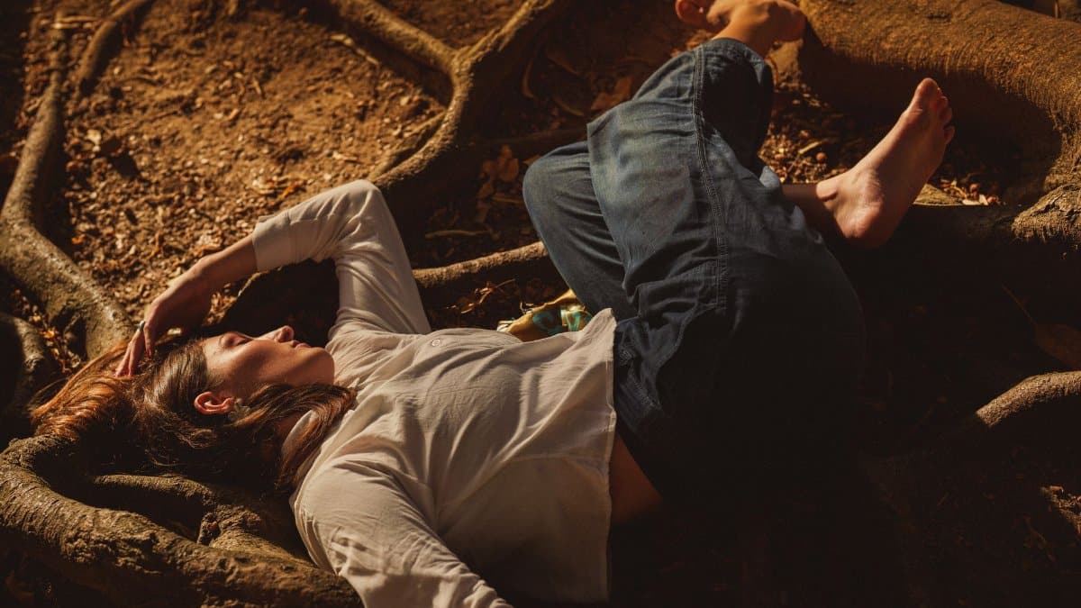 Person calmly resting on tree roots in a sunlit forest setting.
