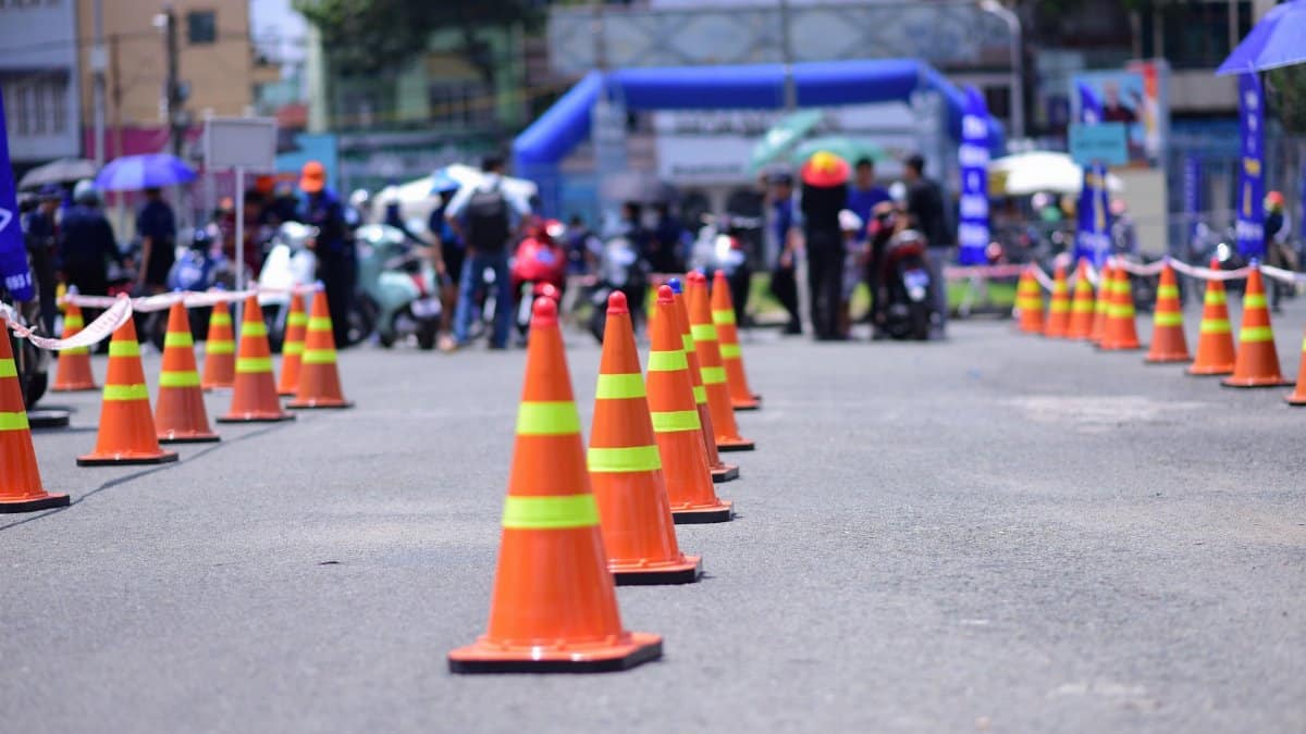Outdoor event with lined traffic cones and blurred people in the background on a sunny day.