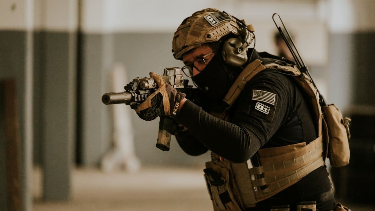 A soldier in tactical gear aims a rifle during indoor military training.