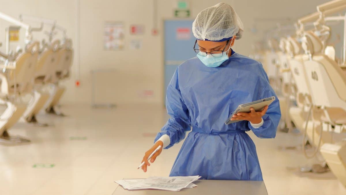 A healthcare professional in blue protective gear reviews documents in a medical clinic.