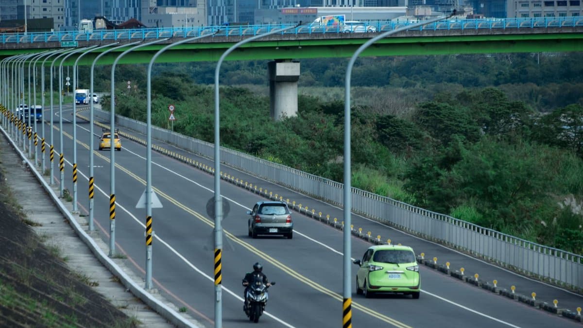 A busy urban highway with cars and motorcycles, featuring a green overpass.