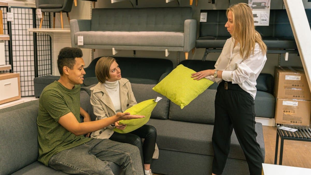 A couple selecting cushions with a salesperson in a furniture store, surrounded by sofas.