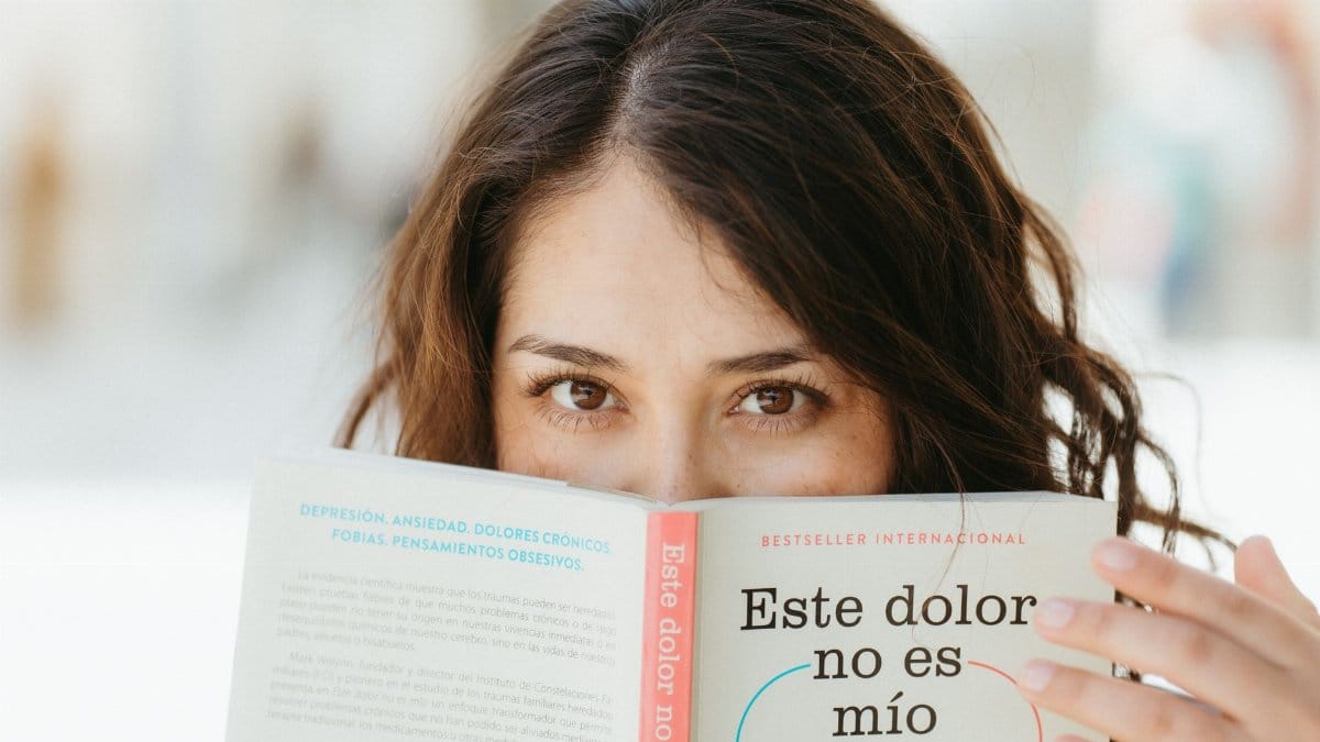 A woman reading a book titled 'Este dolor no es mío', focusing on mental health awareness.