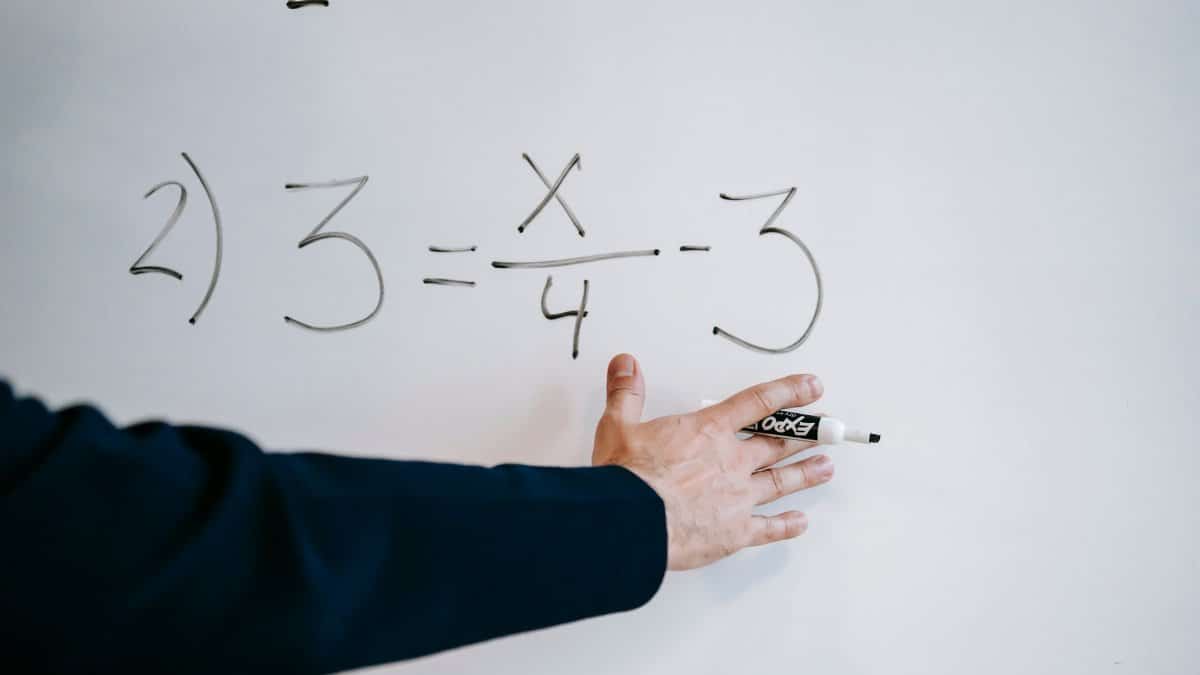 A hand writing a mathematical equation on a whiteboard with a marker.