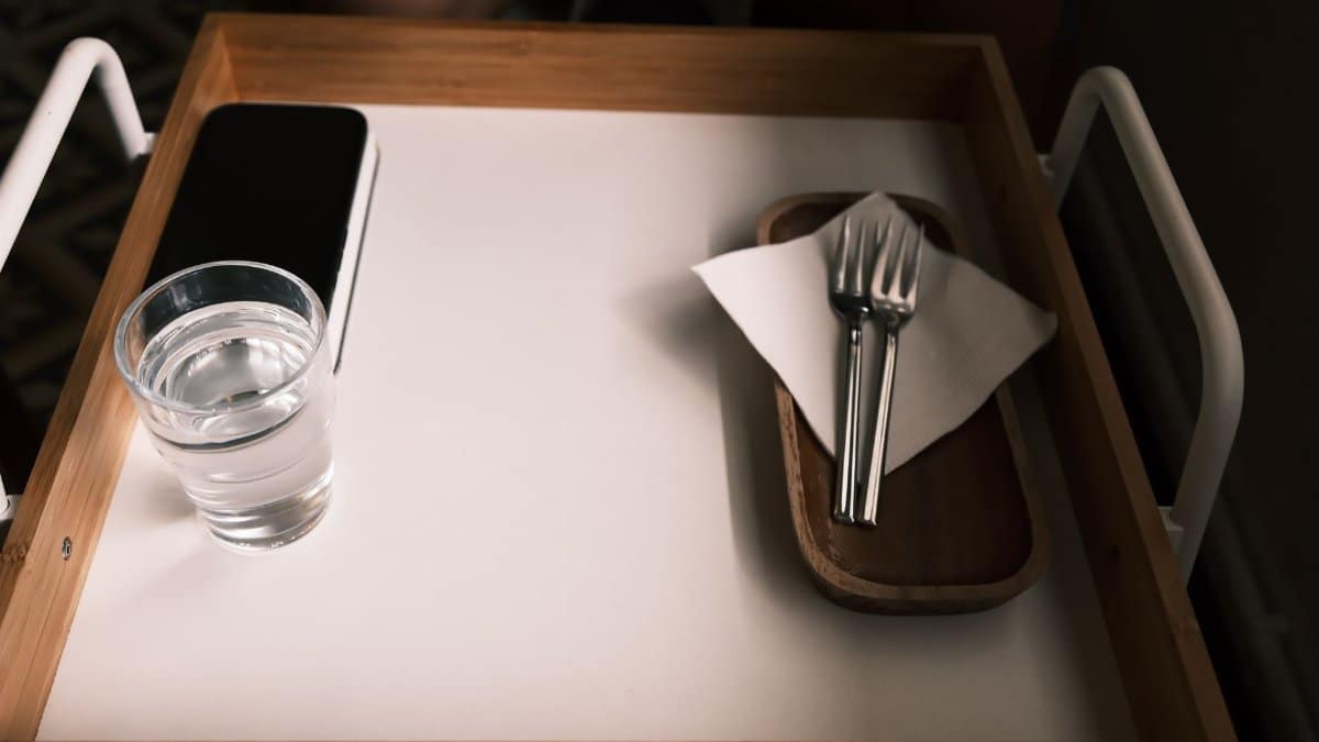 Minimalist wooden tray with glass of water and utensils on white surface.