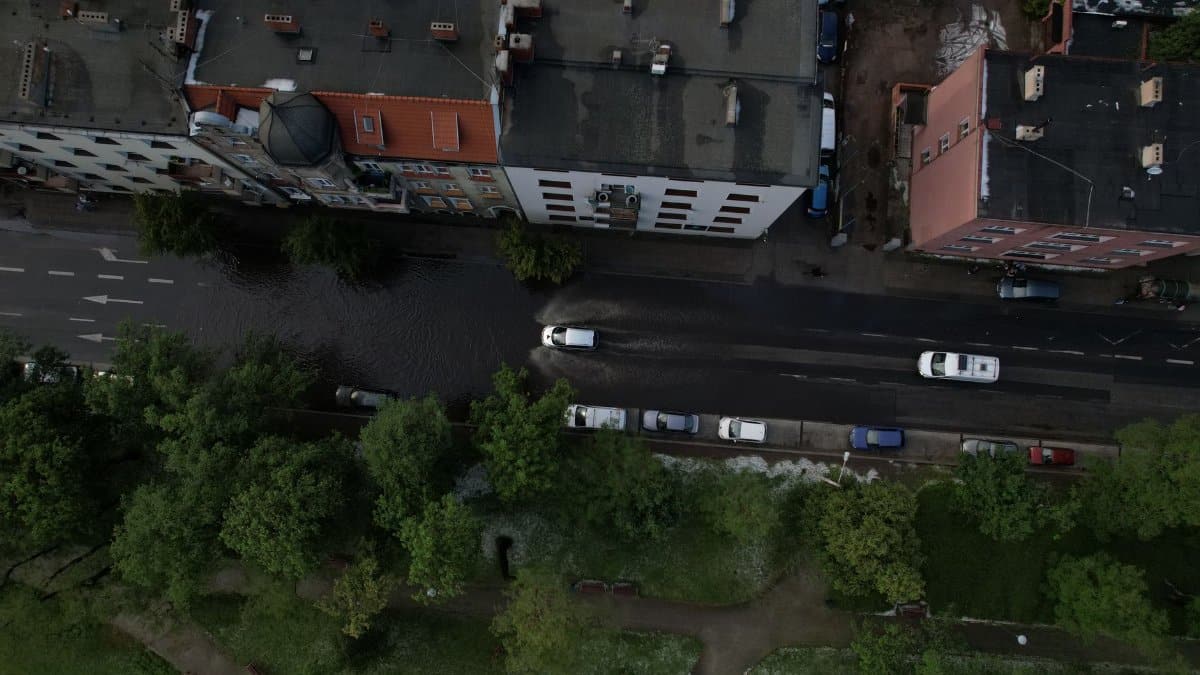 Cars navigate through a flooded street in an urban area, captured from above.