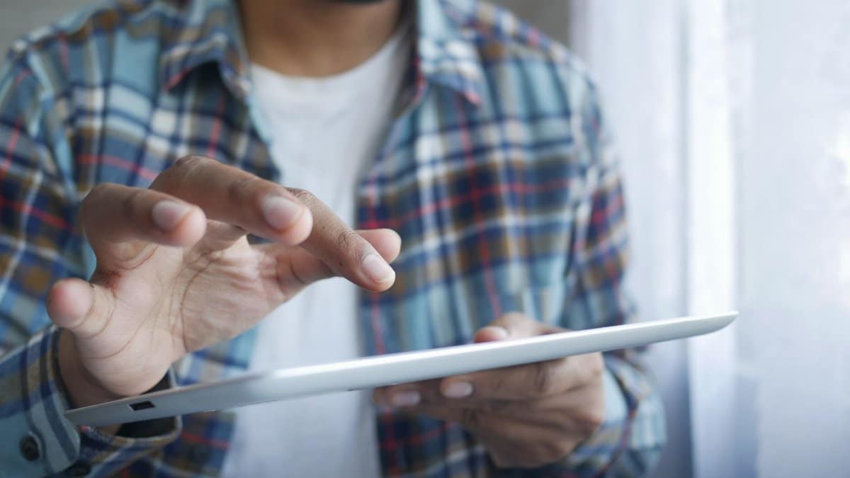 A man in a plaid shirt using a digital tablet indoors, highlighting modern technology in the workplace.