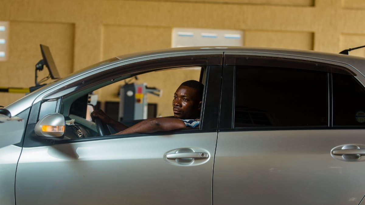 A man sits in a car during a vehicle inspection in a garage setting.
