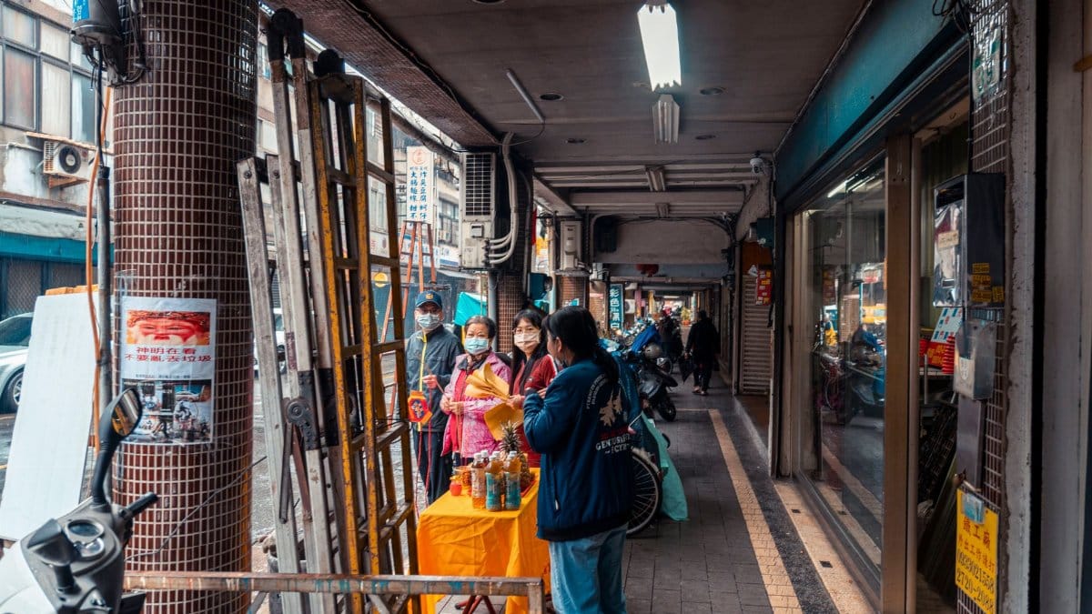 Street market in Asia with vendors and shoppers wearing face masks, showcasing daily life.