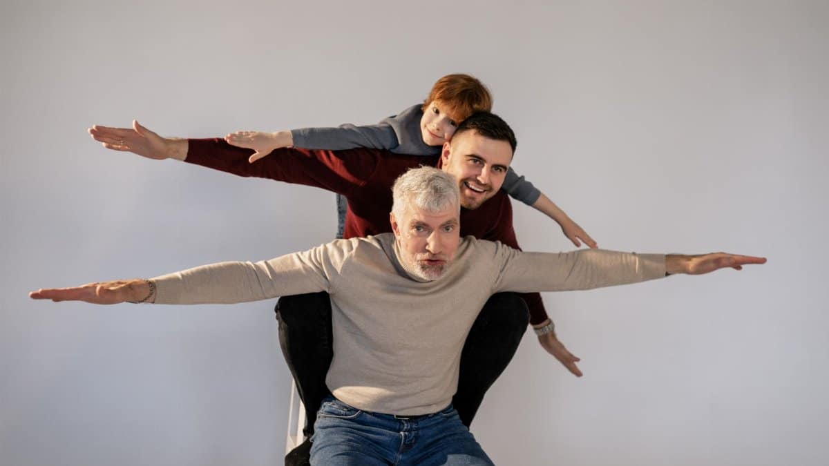 Three generations posing with outstretched arms in a playful studio shoot.