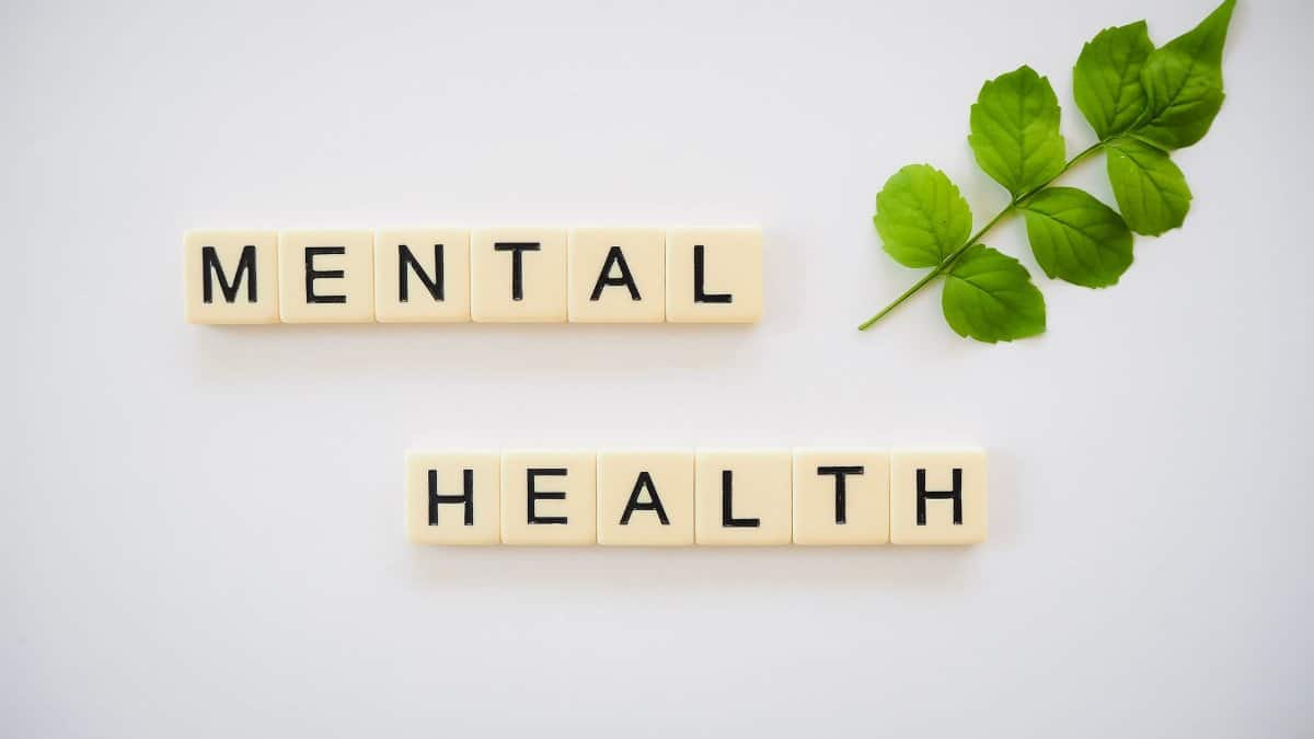 Scrabble tiles spelling 'Mental Health' with green leaves on a white background.