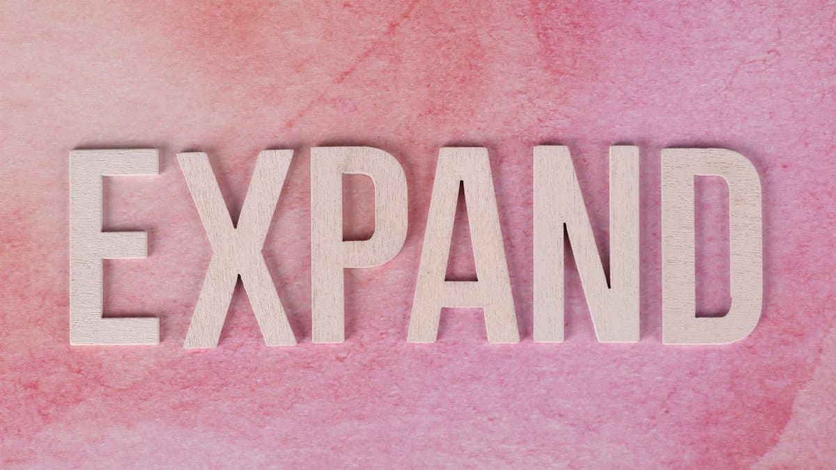 Wooden letters spelling 'EXPAND' on a pink textured background, symbolizing growth and creativity.