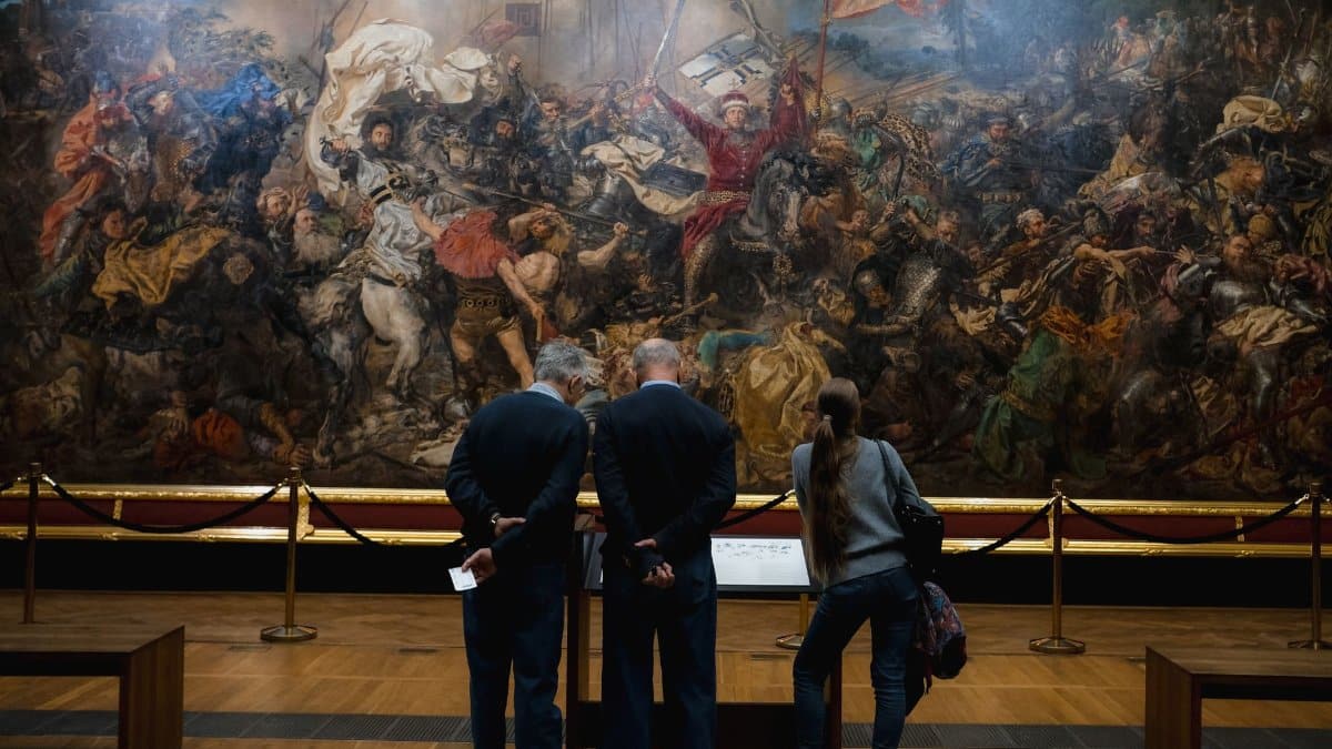 People viewing a large, detailed historical battle painting in a museum setting.