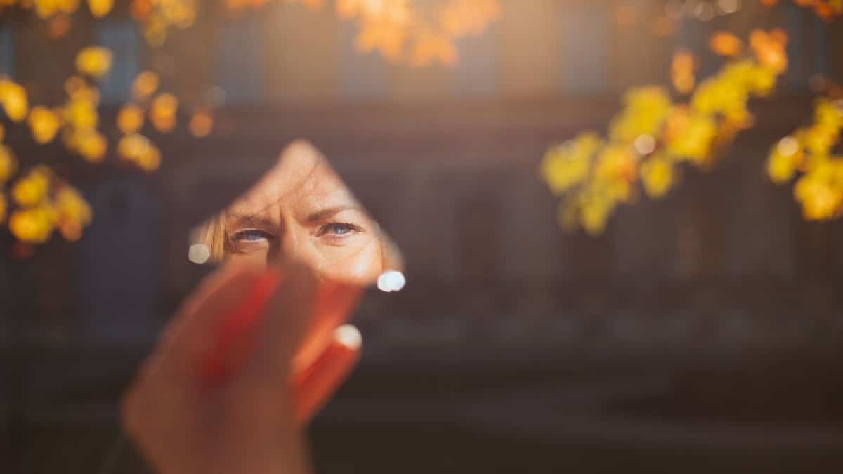 A person holding a mirror reflects autumn leaves in a München park.