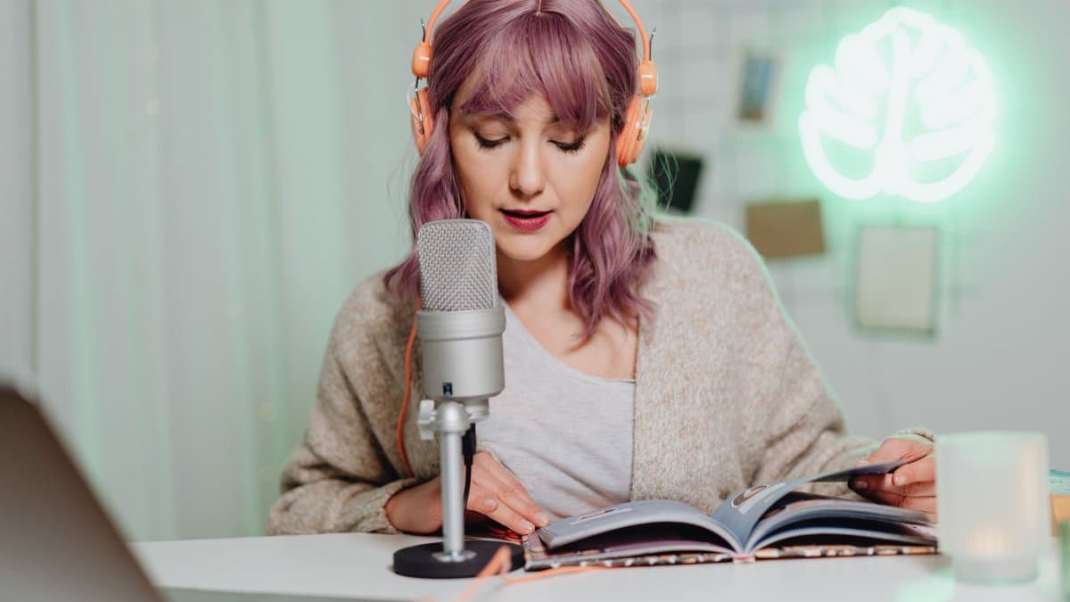 Casual indoor podcast recording featuring a woman with headphones reading from a book.