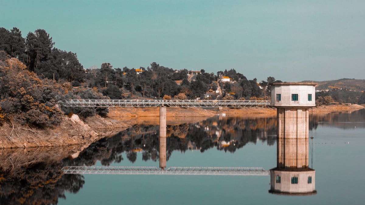 A peaceful lakeside scene showcasing a reflective intake tower and bridge against a forested backdrop.