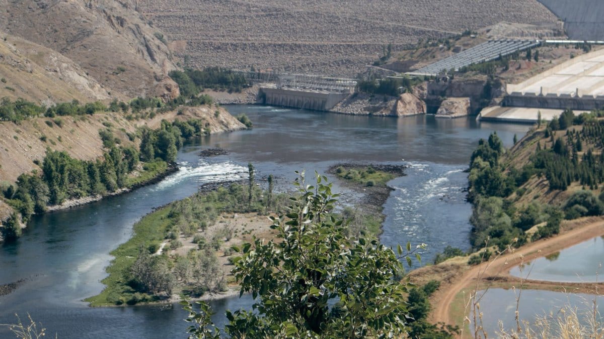 A beautiful view of a river with flowing water, surrounded by mountains and a dam in the distance.