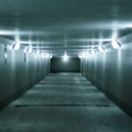 An eerie, dimly lit underground tunnel with fluorescent lights lining the walls, creating a moody atmosphere.