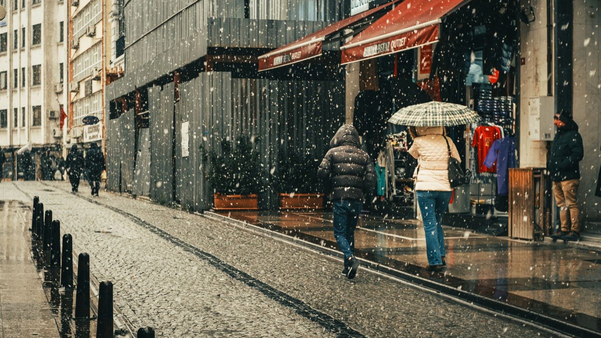 Two people walk under an umbrella during a snowy day in a city street.