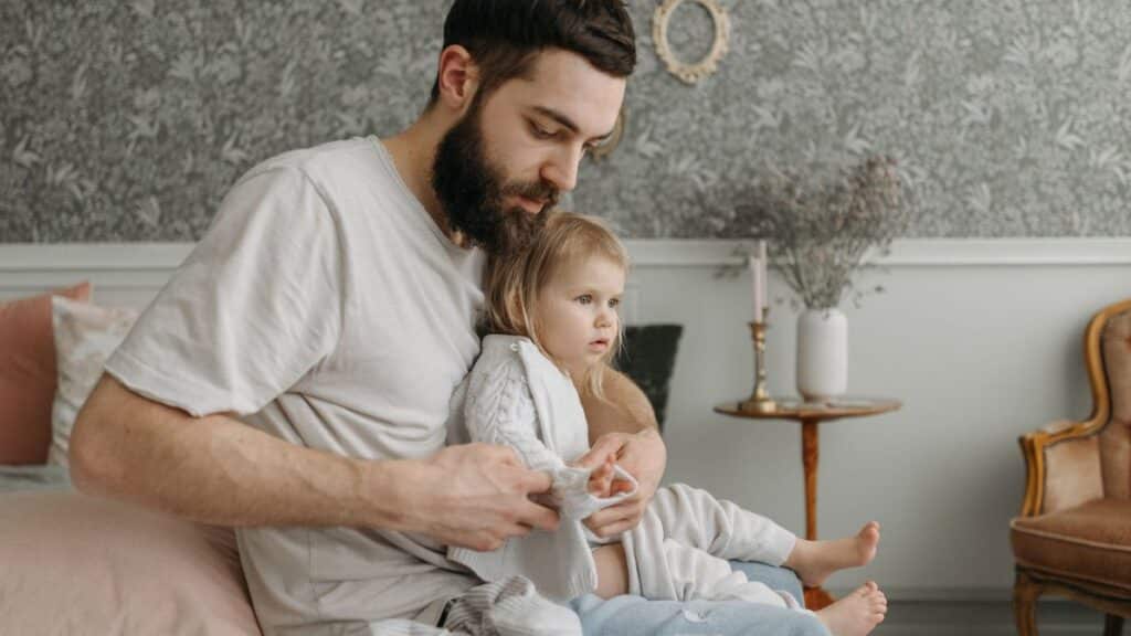 Father helping daughter get dressed in a cozy bedroom environment, highlighting nurturing parenting moments.