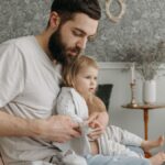 Father helping daughter get dressed in a cozy bedroom environment, highlighting nurturing parenting moments.