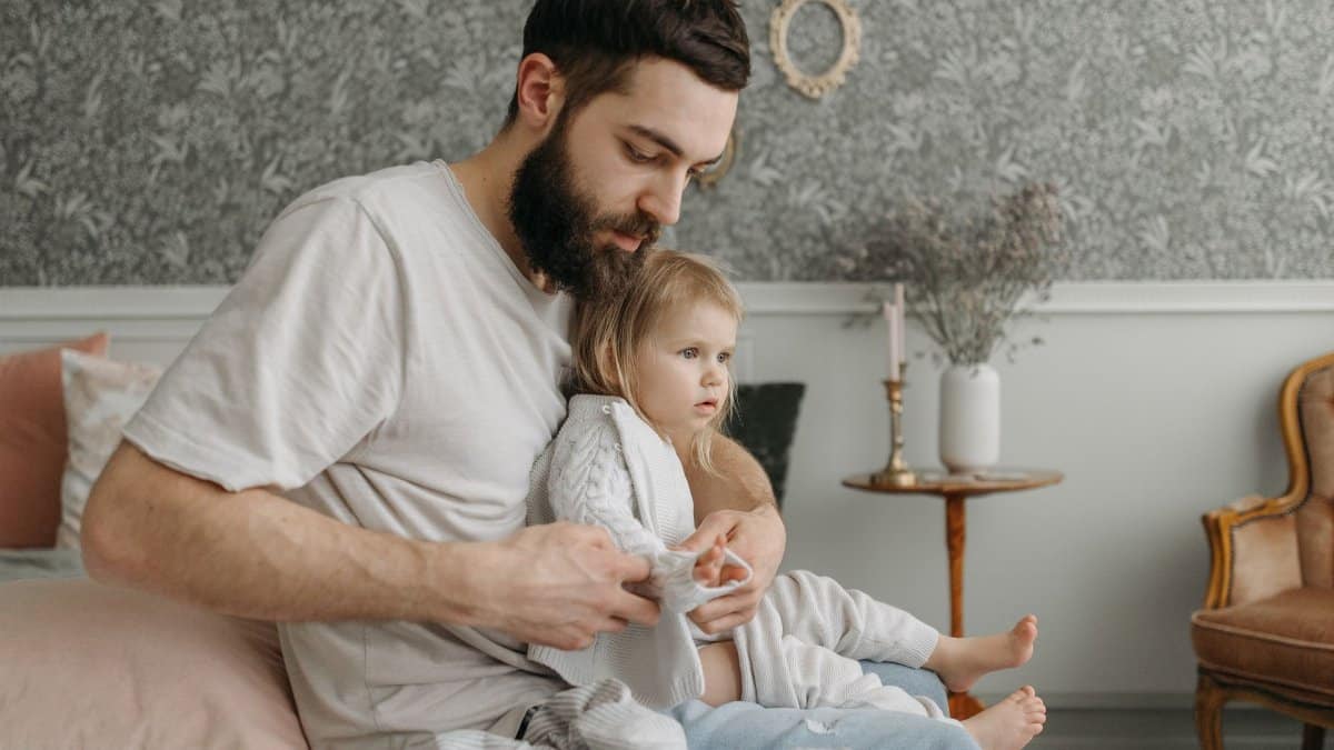 Father helping daughter get dressed in a cozy bedroom environment, highlighting nurturing parenting moments.