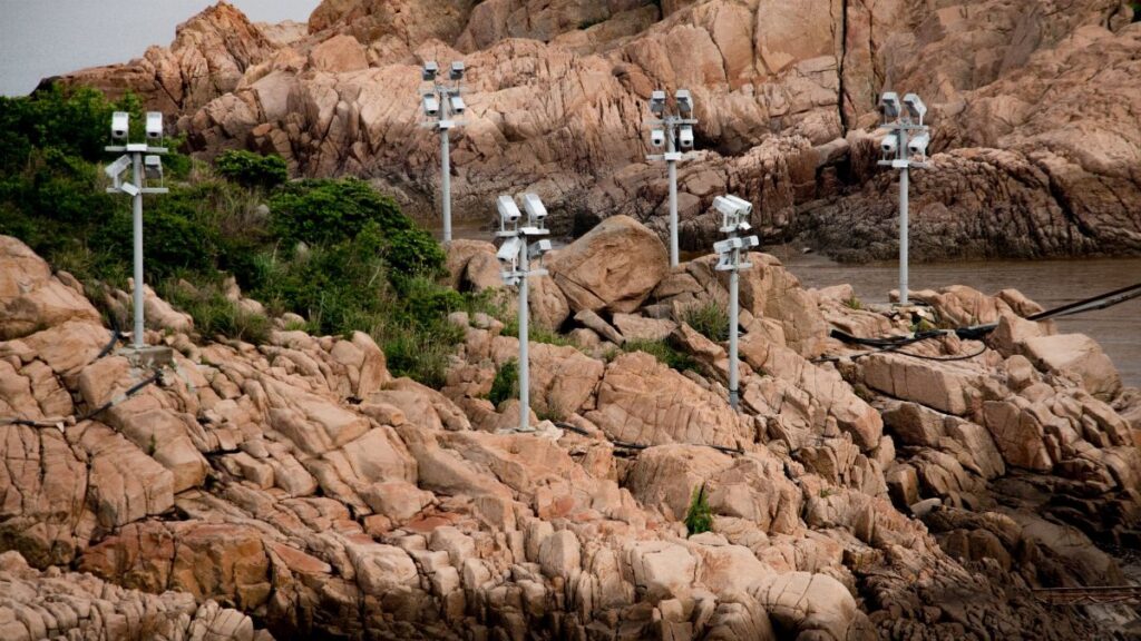 Multiple surveillance cameras monitor a rocky coastline with surrounding vegetation.