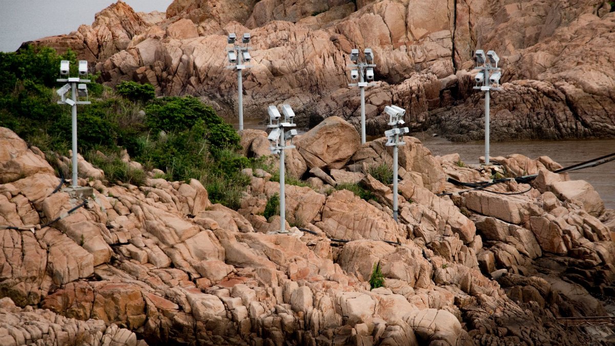 Multiple surveillance cameras monitor a rocky coastline with surrounding vegetation.