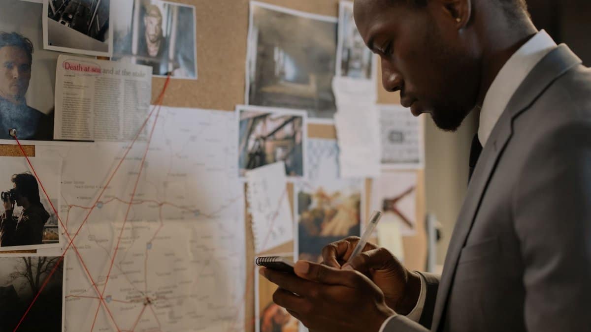 Man in a suit investigating a crime scene board, taking notes and analyzing evidence.