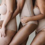 Three diverse women hugging, showcasing body positivity and diversity in nude bodysuits.