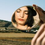 Young Woman Holding a Little Mirror and Standing on a Field