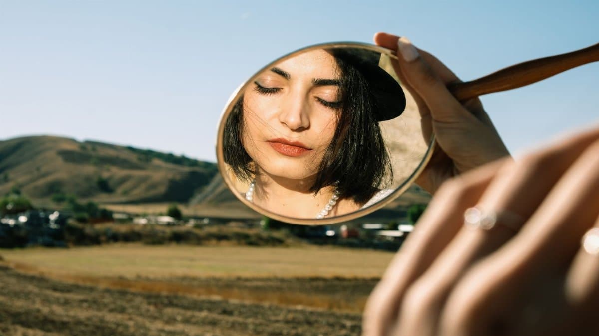 Young Woman Holding a Little Mirror and Standing on a Field