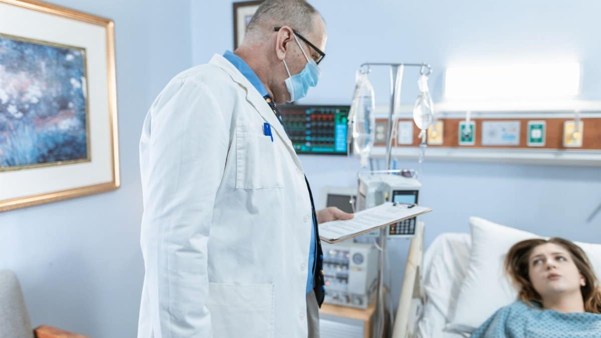 Doctor checks on patient in hospital room with medical equipment.