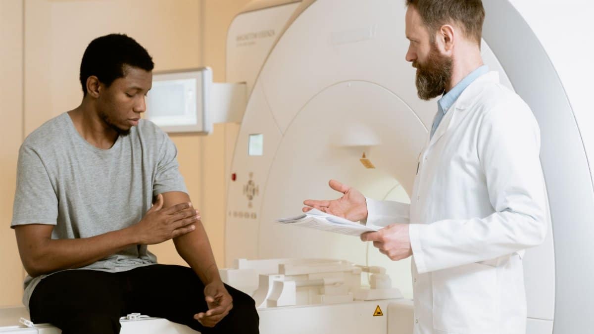 A doctor consults with a patient by an MRI scanner in a medical facility.