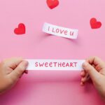 Hands holding love notes on pink background with red hearts. Perfect for Valentine's Day.