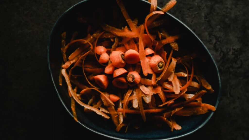 Close-up photo of fresh carrot peels and scraps in a dark bowl, perfect for food waste or preparation themes.